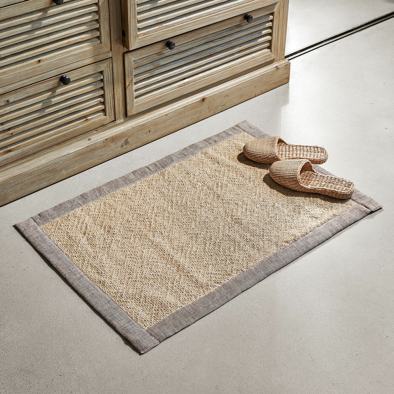 Badmat Wilder Beige vloerkleed van natuurlijk materiaal met grijze rand op lichte vloer bij houten kast