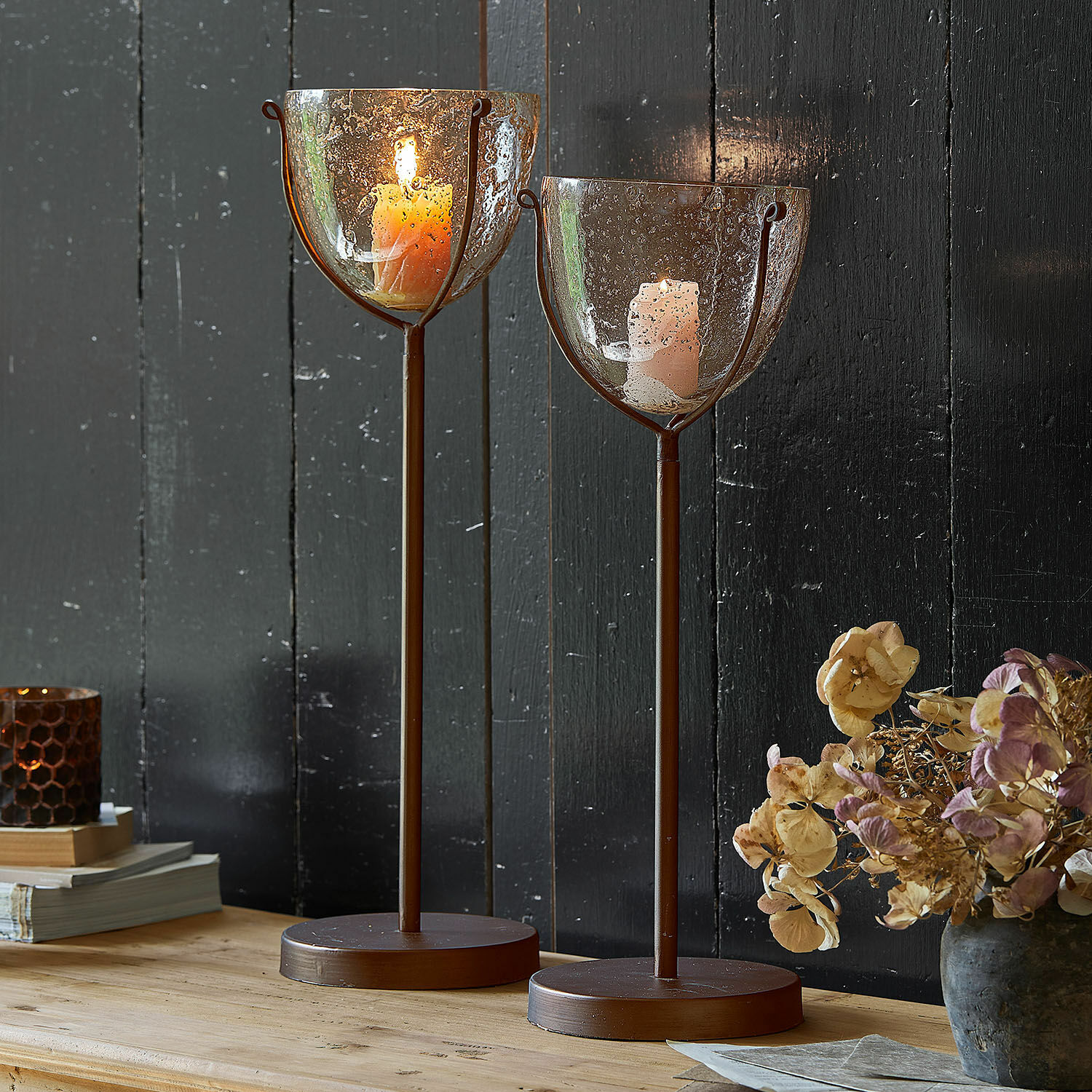 Kaarsenstandaard set van 2 Piacello Twee bruine metalen kandelaren met bubbeltjesglas en brandende kaarsen op houten tafel