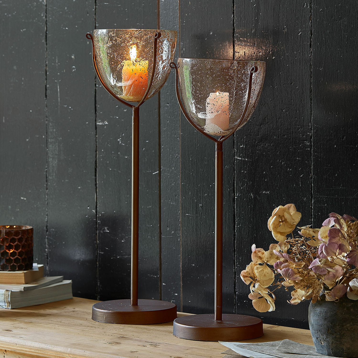 Kaarsenstandaard set van 2 Piacello Twee bruine metalen kandelaren met bubbeltjesglas en brandende kaarsen op houten tafel