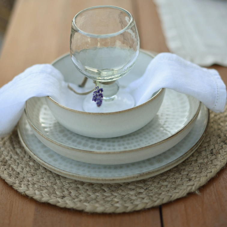 Set wit keramisch servies met borden en kom op gevlochten placemat met witte servet