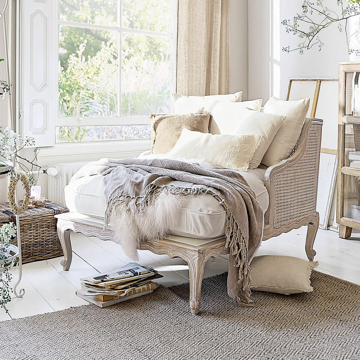 Chaise longue Dronne Beige bank van hout en riet met crèmekleurige kussens en zachte deken in lichte kamer