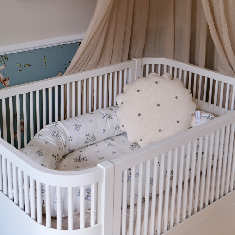 Lit bébé blanc avec coussin doux et linge de lit à motif floral dans des tons pastel