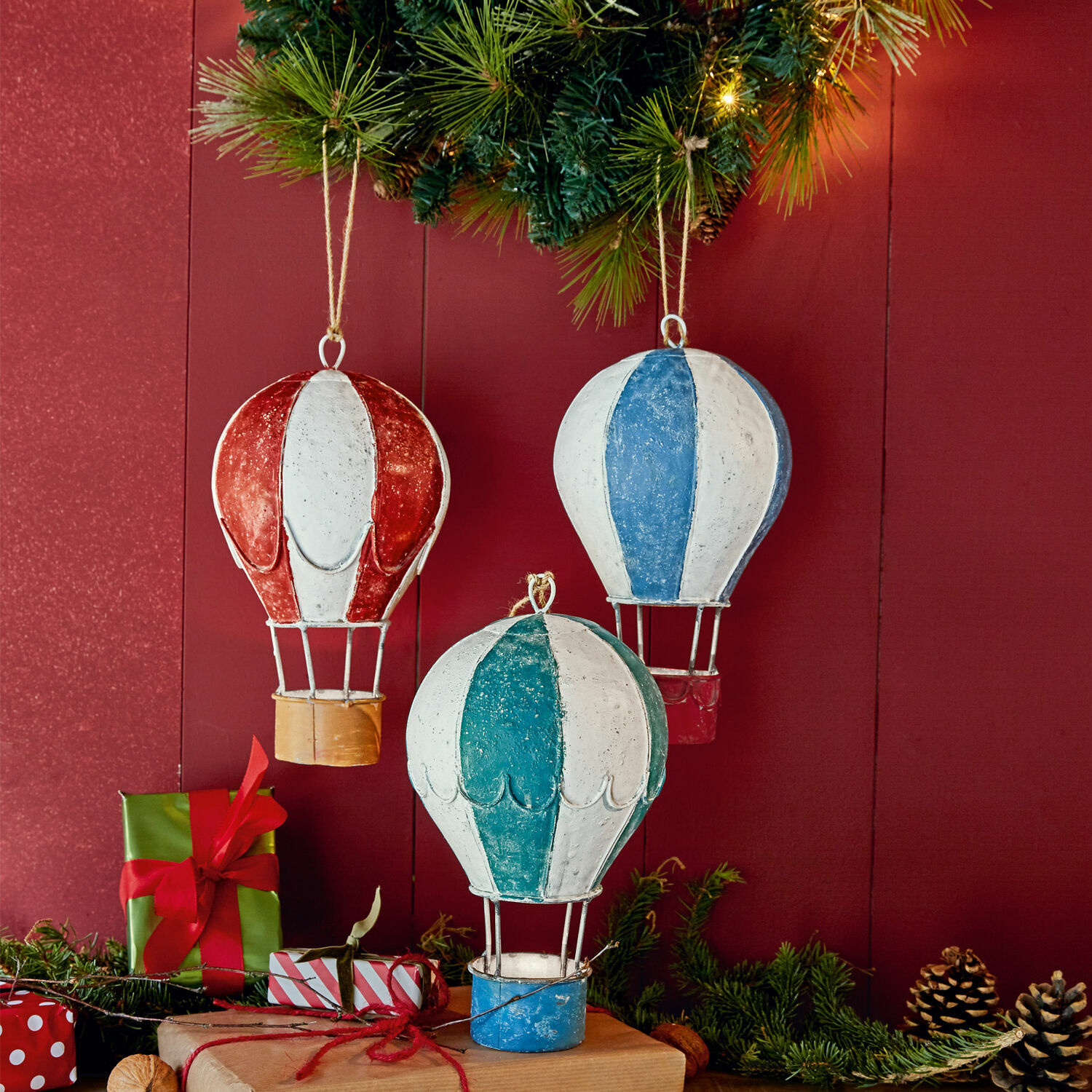 Décorations métalliques en forme de montgolfières sur fond rouge avec branches vertes et cadeaux