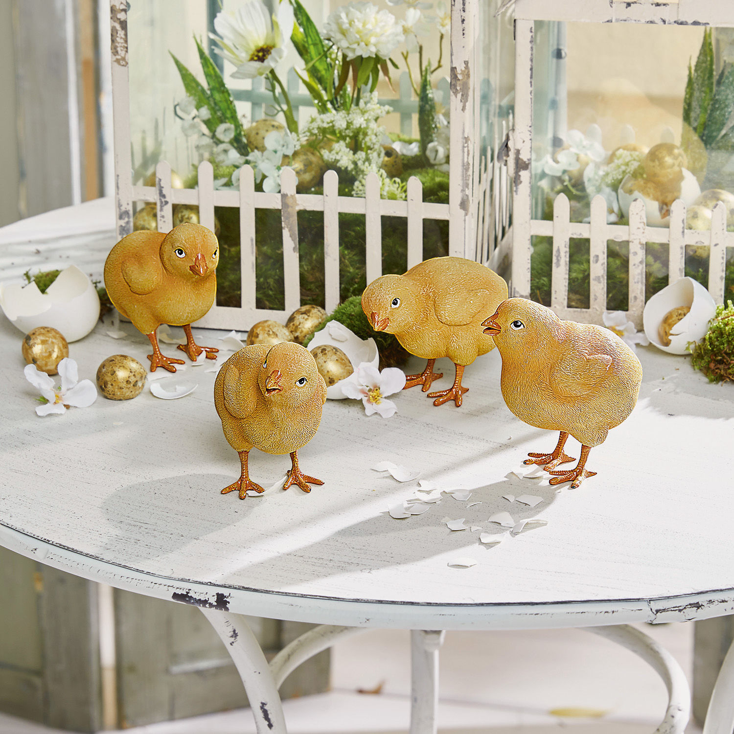 Quatre poussins décoratifs jaunes sur une table blanche avec décorations de Pâques et œufs artificiels