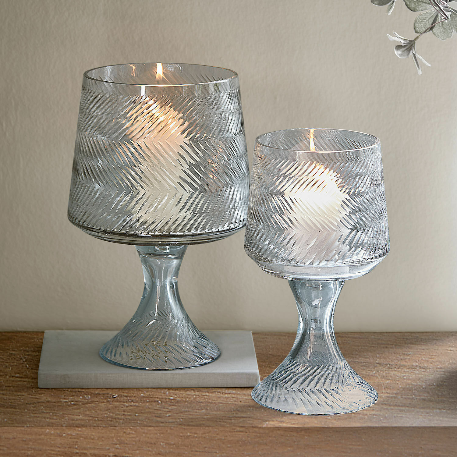 Lot de 2 photophores Lynettes Deux photophores en verre transparent avec motif en relief et bougies blanches sur une table en bois