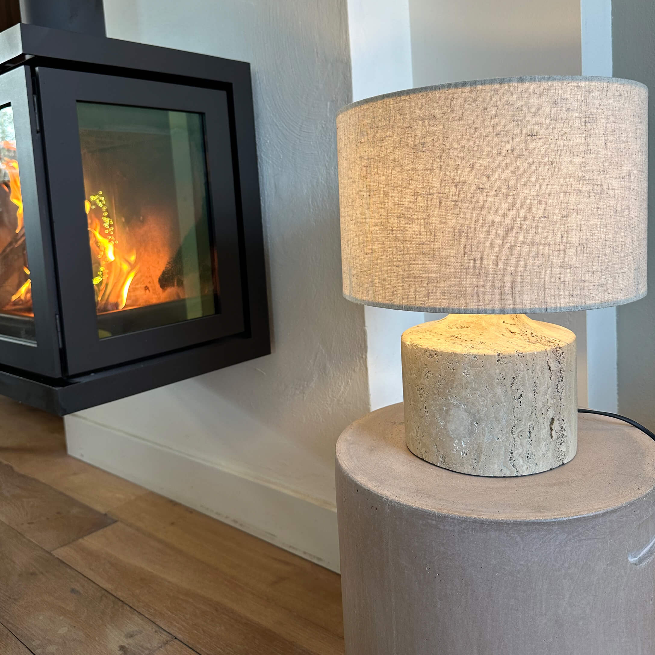 Lampe de table avec abat-jour beige et base en pierre claire près d'une cheminée allumée