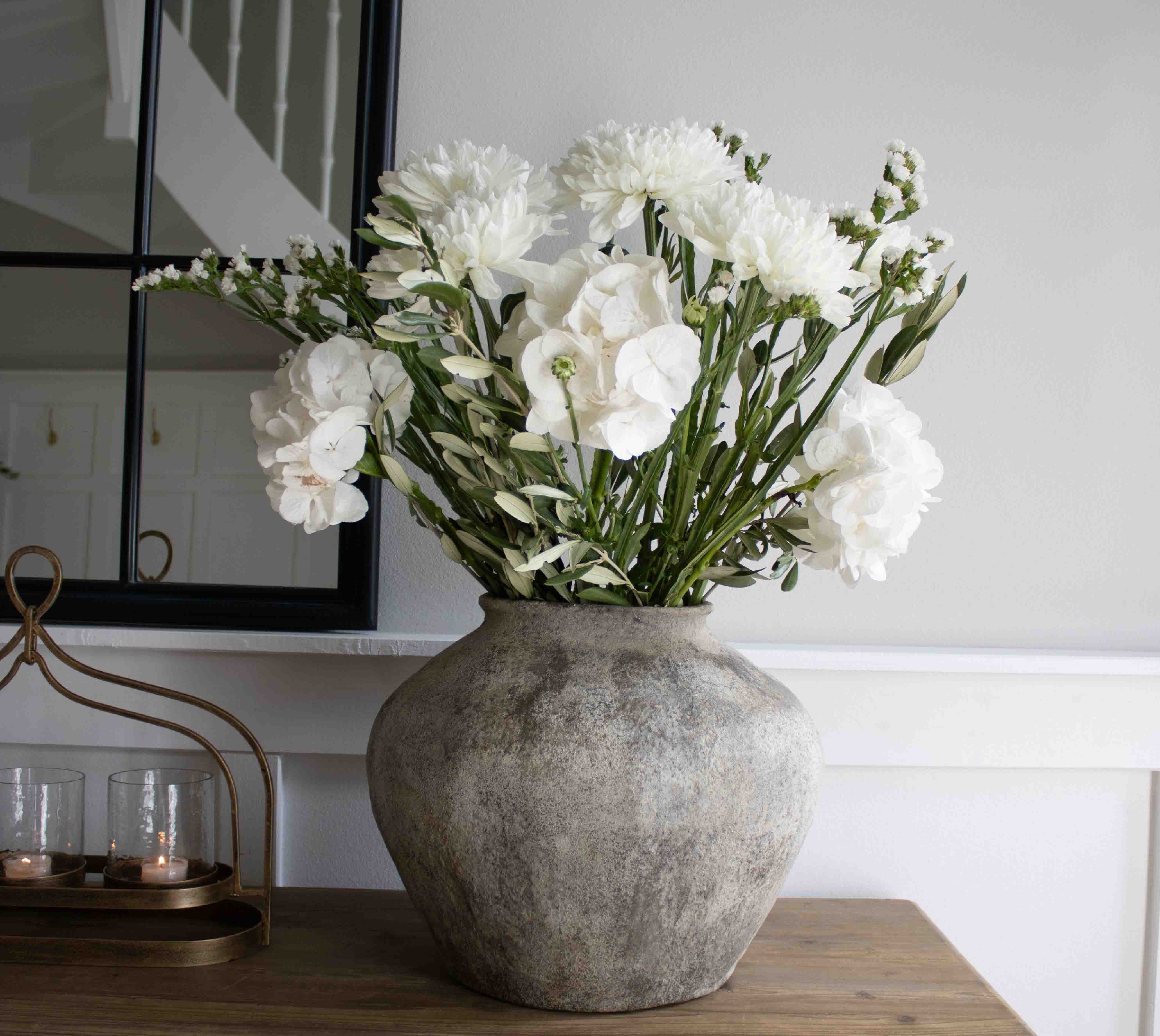 Grote grijze stenen vaas met witte decoratieve bloemen op houten tafel in woonkamer