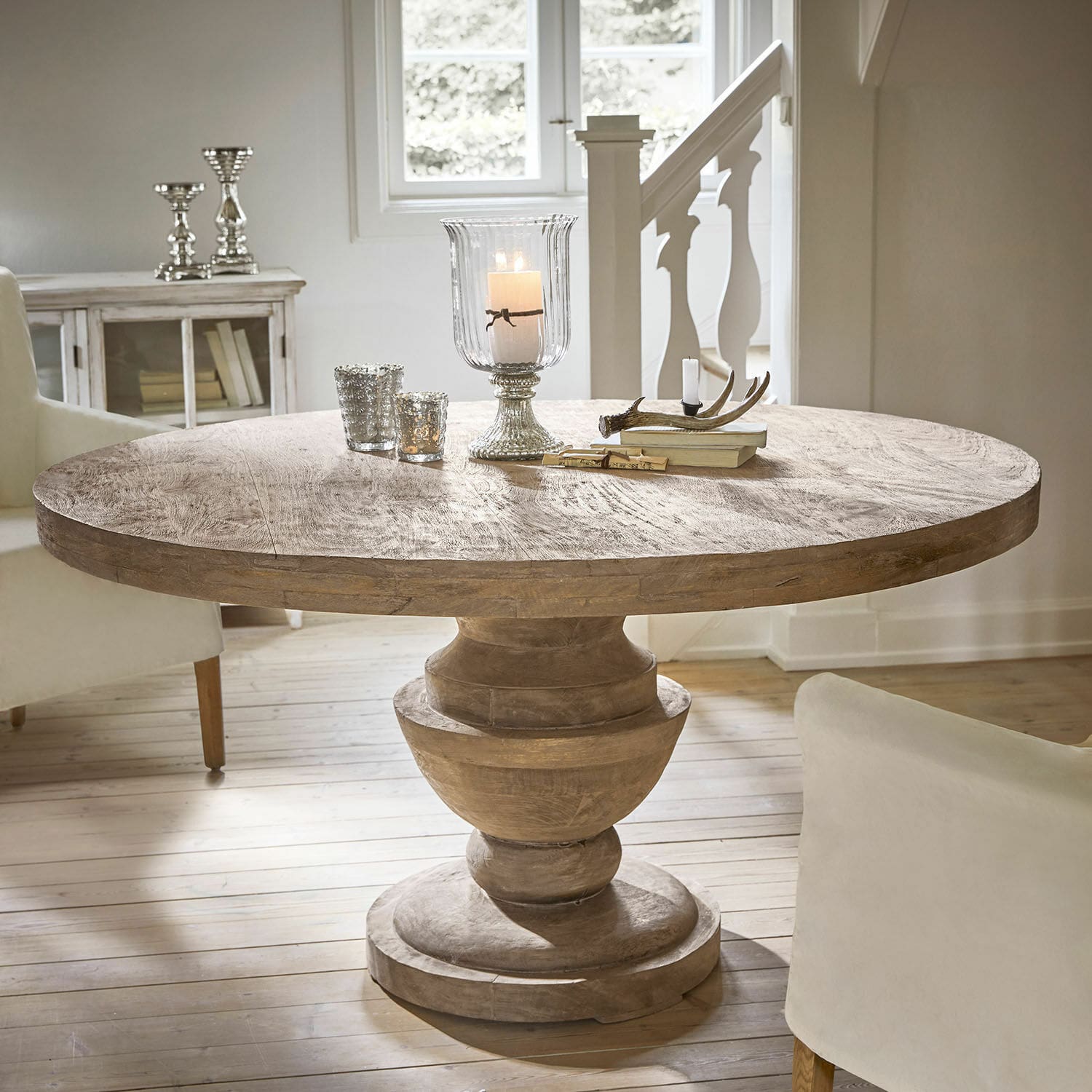 Tafel Retonfey Ronde mangohouten tafel in natuurlijke kleur met decoratieve kandelaars en boeken erop in lichte kamer