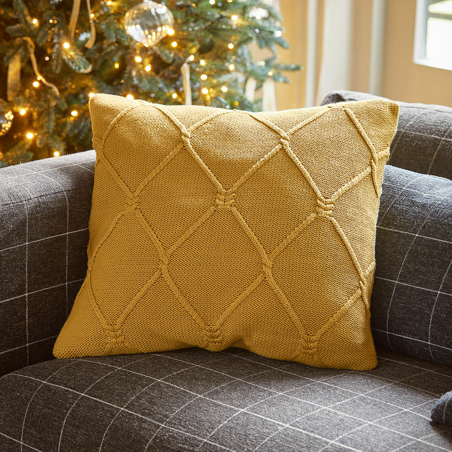 Coussin décoratif moutarde en tricot sur canapé gris à motif carreaux pour salon cosy