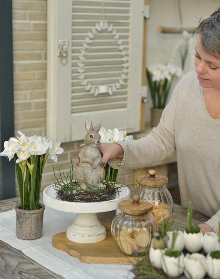 Décoration de Pâques avec figurine de lapin, fleurs blanches et bocaux à biscuits sur une table claire