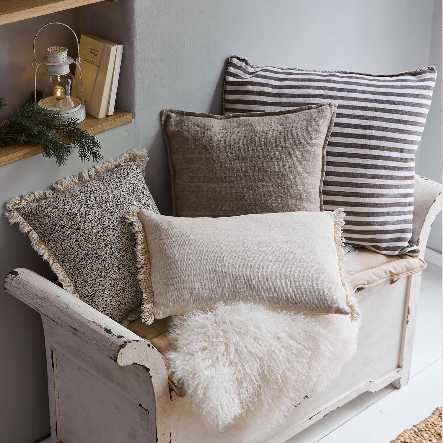 Set decoratieve kussens in beige en bruintinten op een witte houten bank met een zachte bontdeken