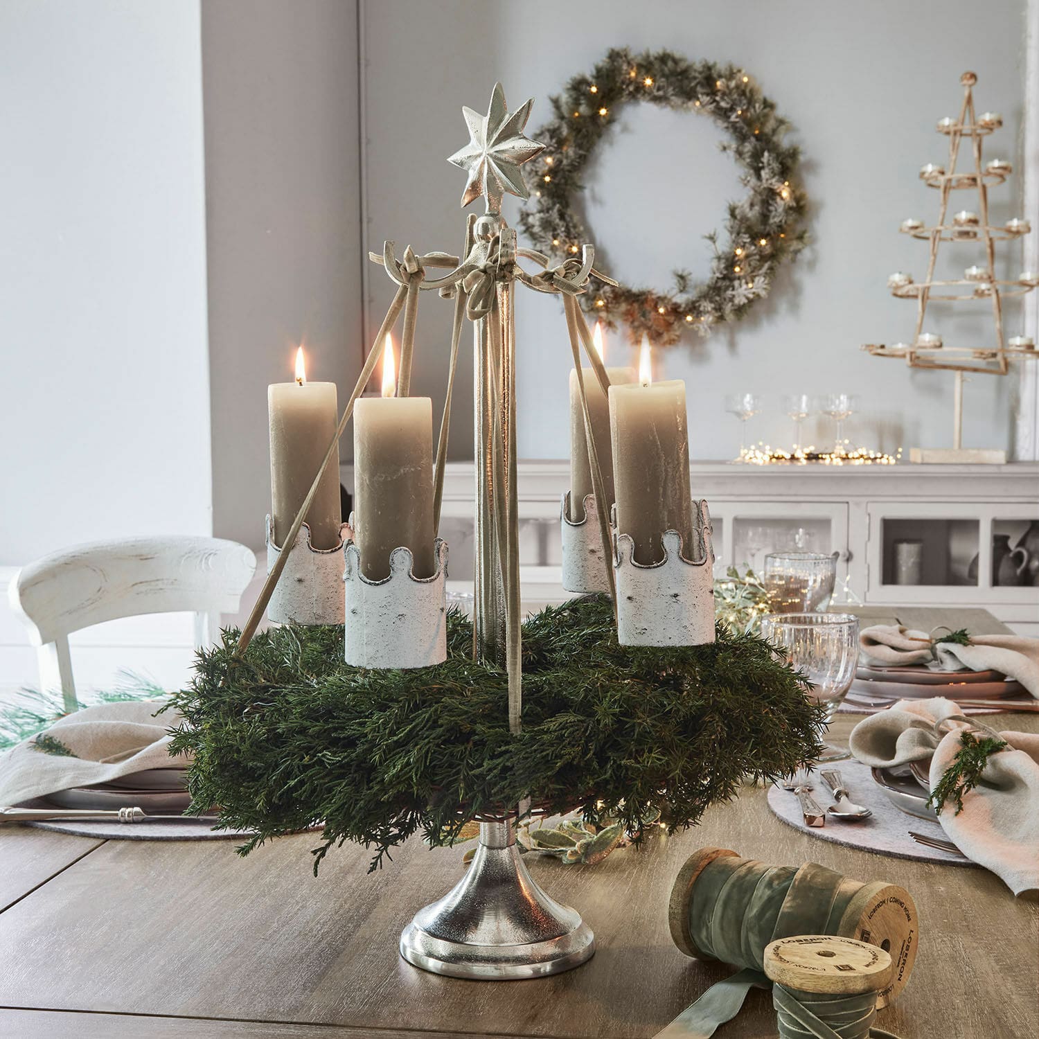 Support pour couronne Graham Couronne de l'Avent en métal avec quatre bougies beige et feuillage vert sur table en bois