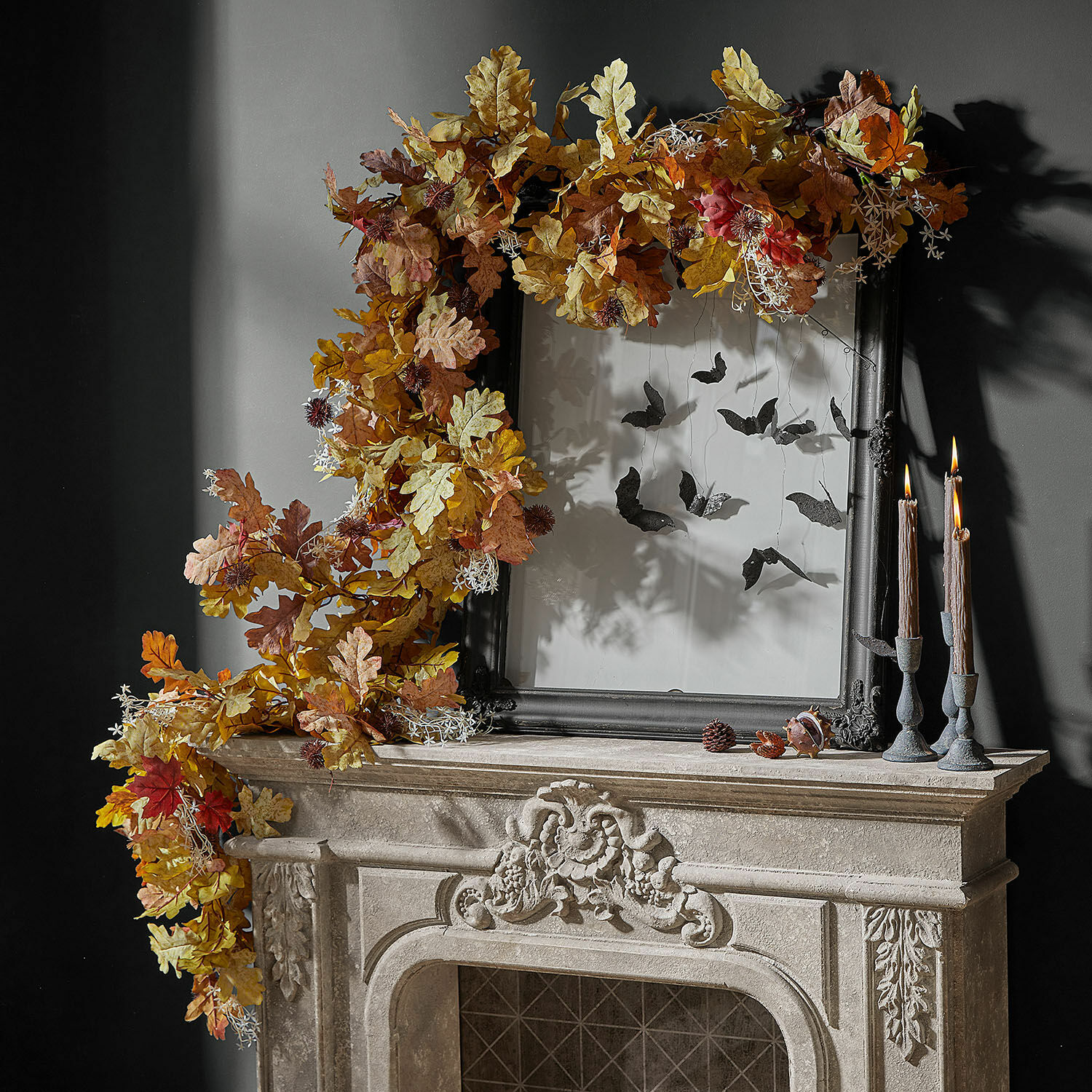 Guirlande Fleurimont Couronne d'automne décorative en feuilles de chêne aux tons chauds sur une cheminée en pierre avec cadre noir et bougies