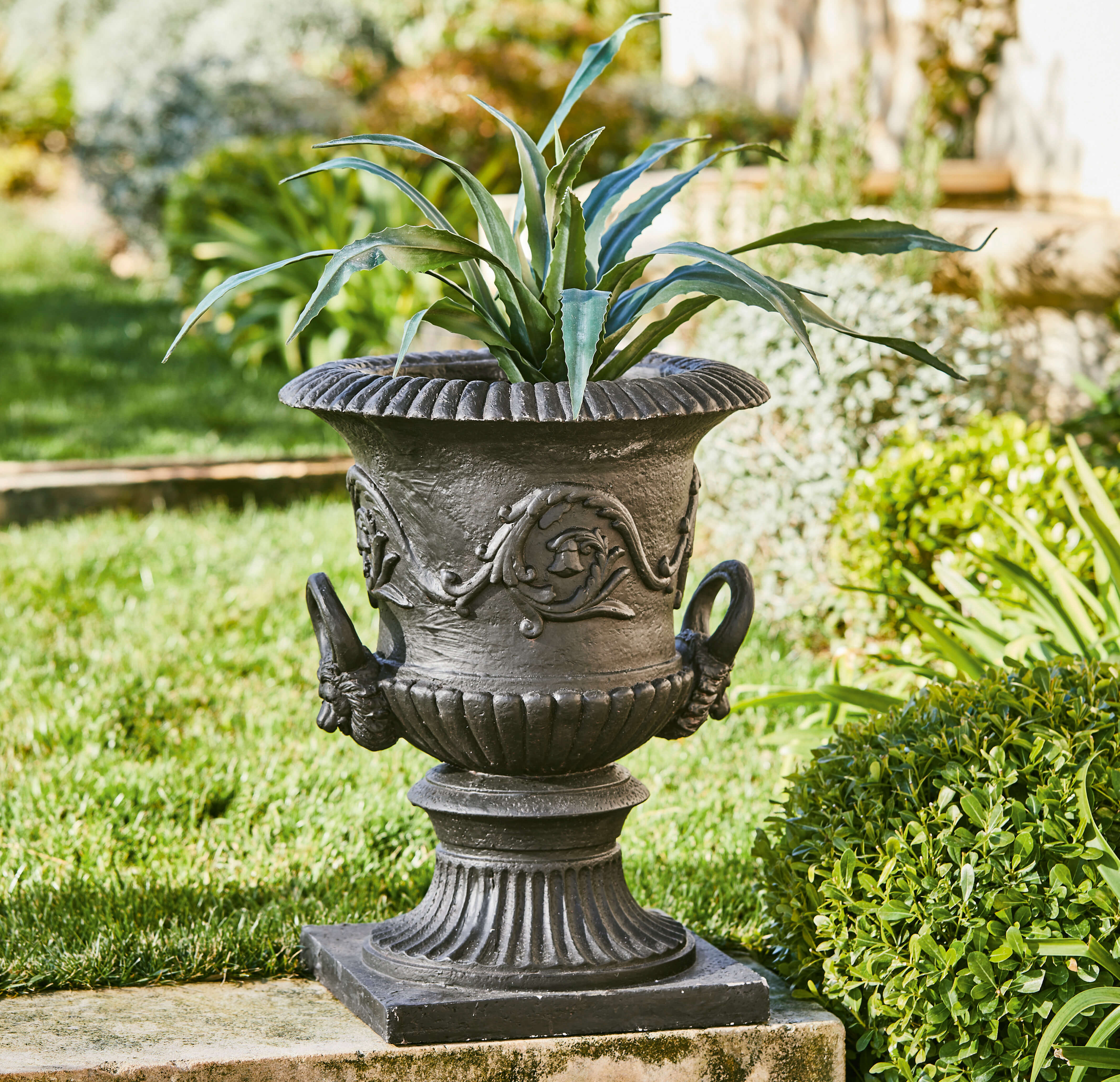 Zwarte sierlijke gietijzeren plantenbak met plantenmotief in klassieke stijl in de tuin