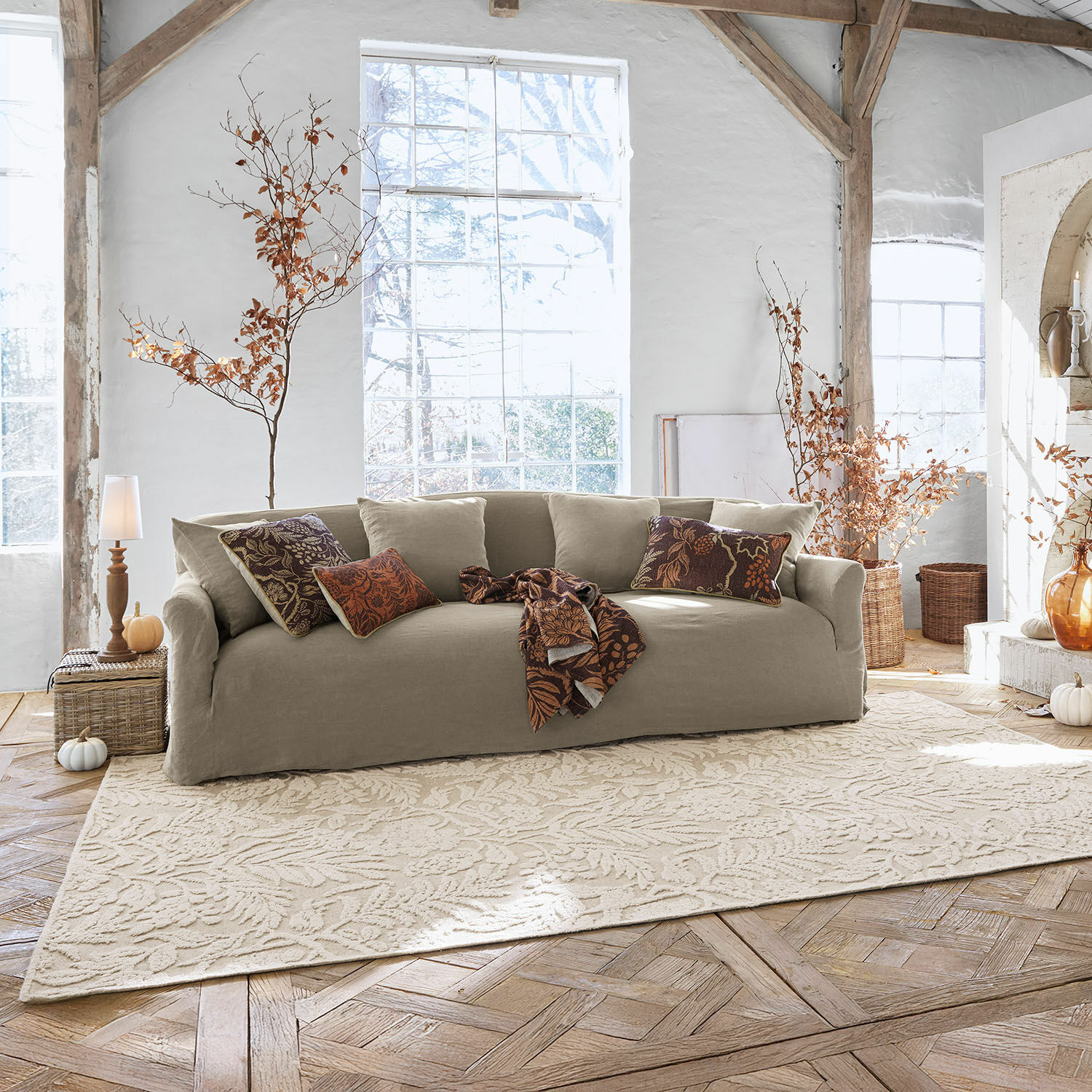 Tapis Azimra Canapé beige en tissu dans un salon lumineux avec coussins décoratifs et tapis à motif feuilles