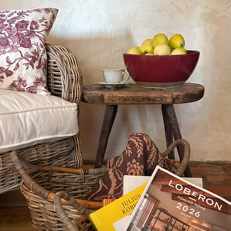 Table en bois rustique avec bol en céramique bordeaux rempli de pommes jaunes à côté d'un fauteuil en osier avec coussin