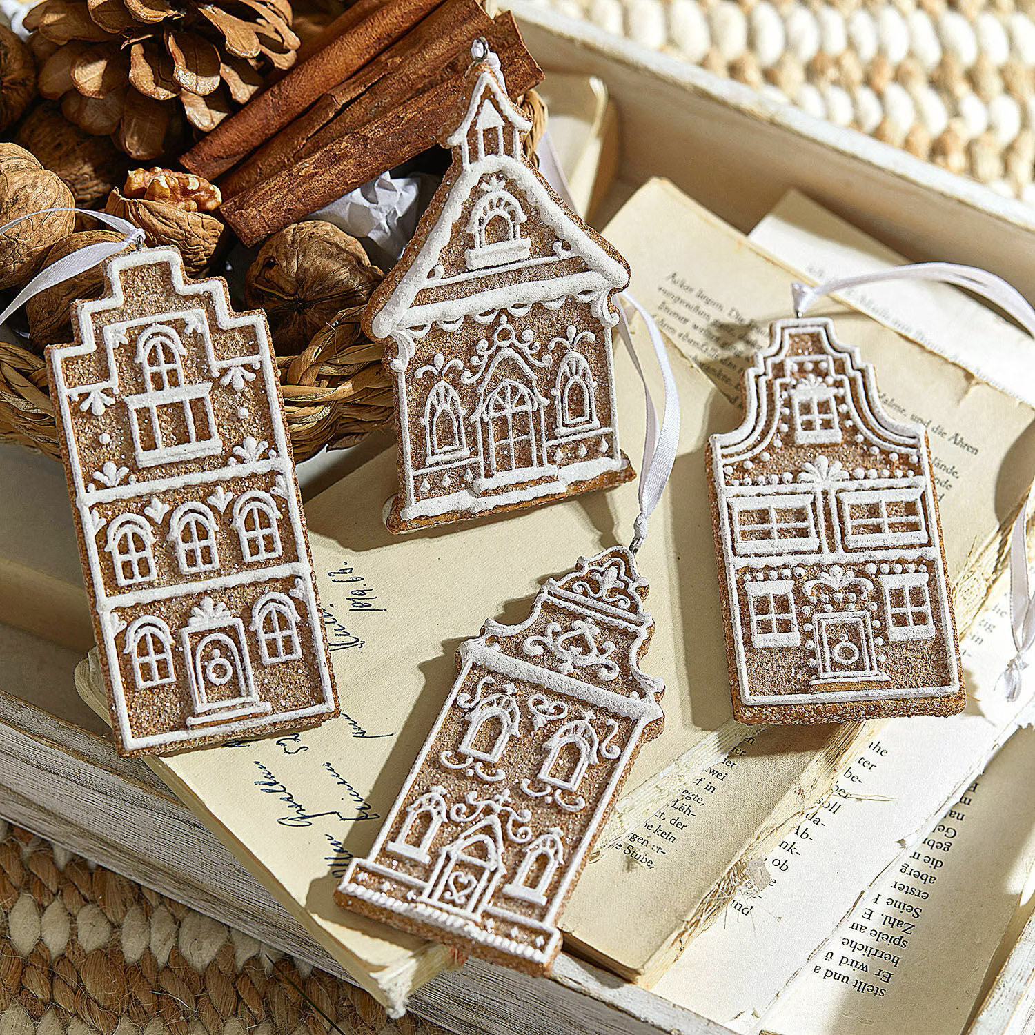 Quatre décorations en pain d'épice en forme de maisons avec glaçage blanc sur des livres anciens et des noix