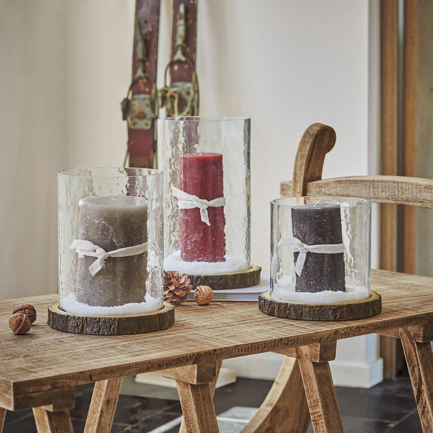 Lot de 3 photophores Malliévre Trois photophores en verre avec base en bois et bougies colorées sur une table en bois, décoration intérieure