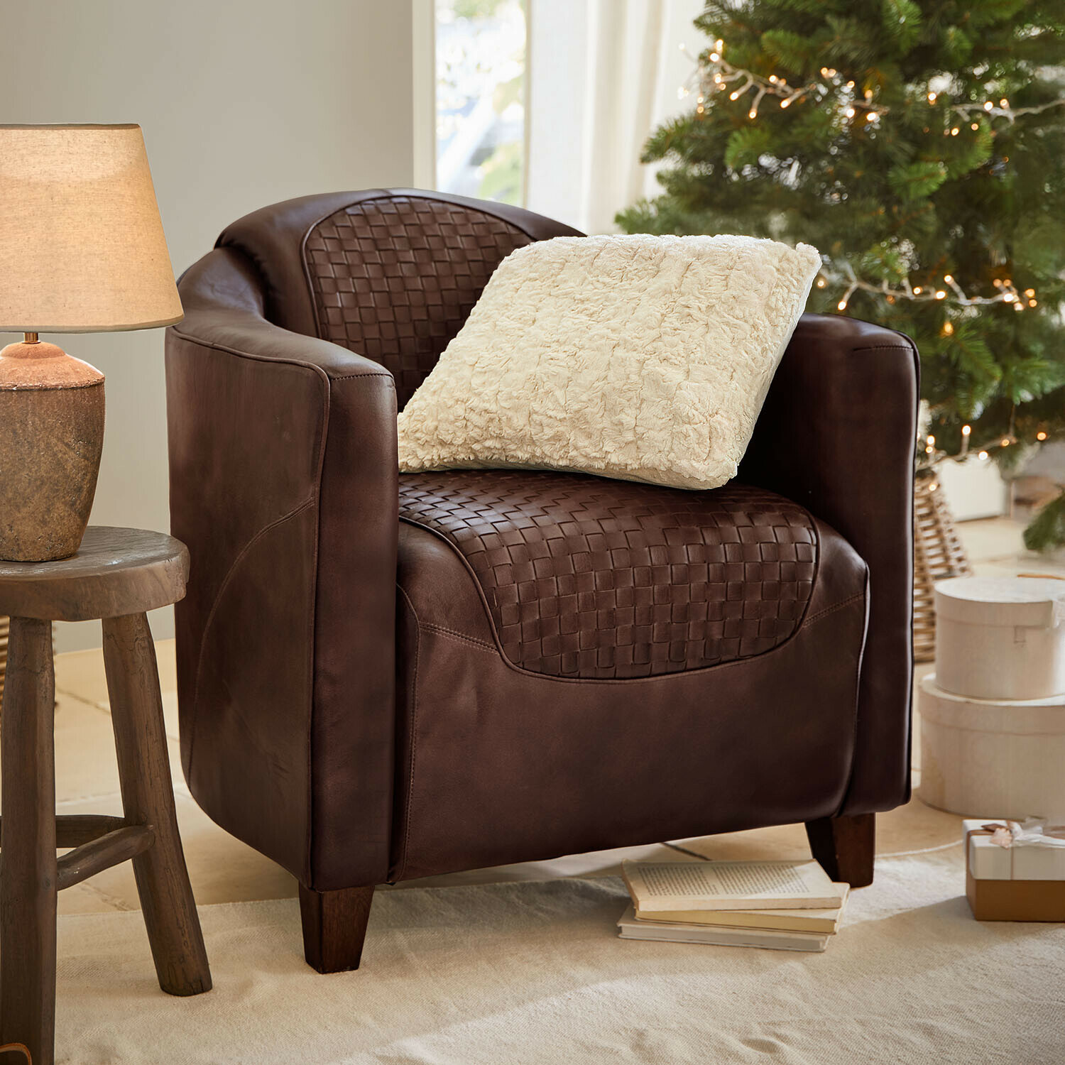 Fauteuil Westerdales Bruine leren fauteuil met gevlochten zitting en crème kussen, gezellige setting met lamp en kerstboom