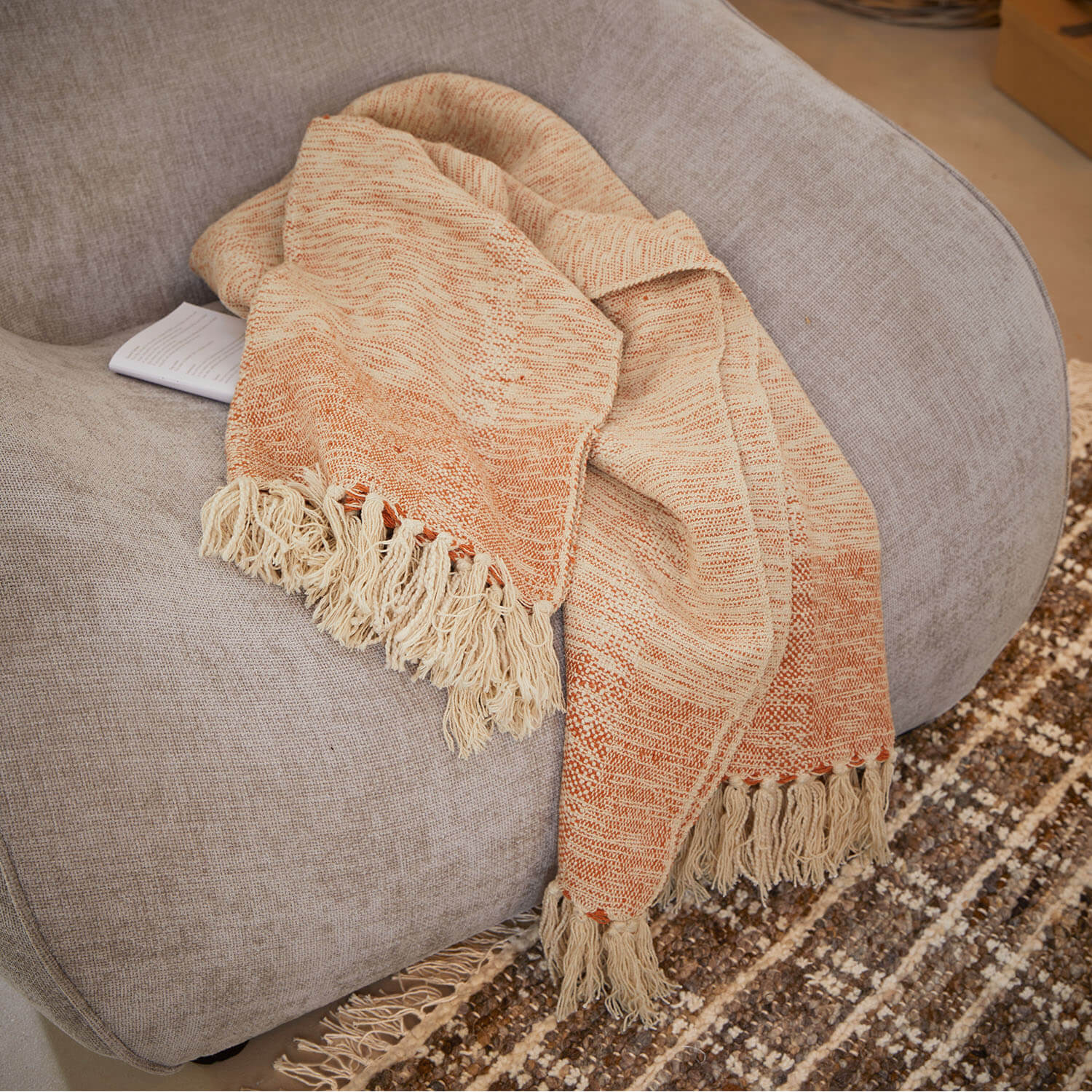 Plaid beige et orange avec franges sur un canapé gris, tissu doux pour décoration intérieure