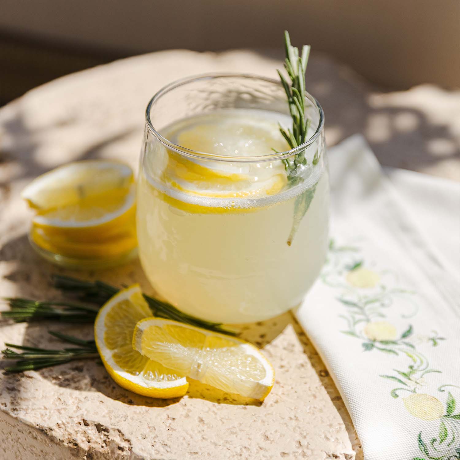 Verre de limonade avec tranches de citron et branche de romarin sur surface en pierre avec serviette