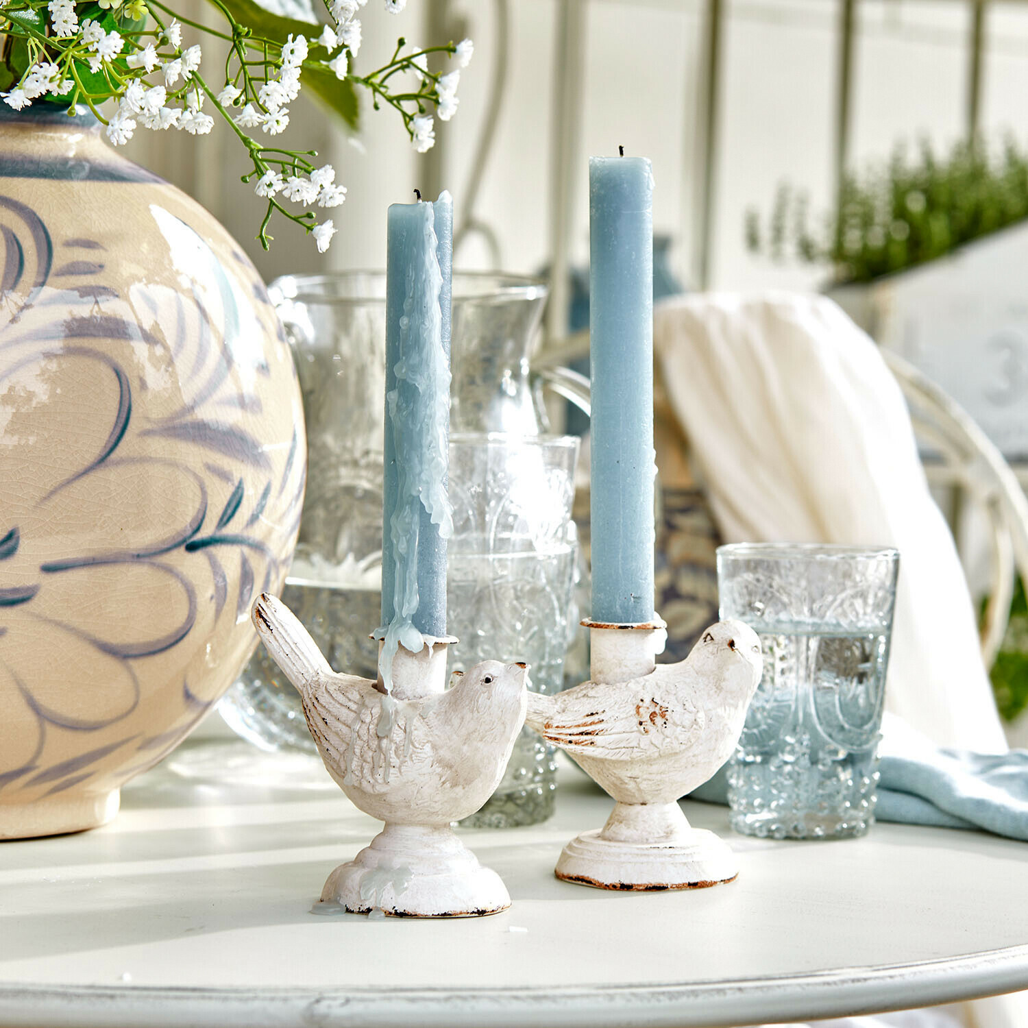 Witte vogelkaarsenhouders met blauwe kaarsen op lichte tafel met bloemendecoratie