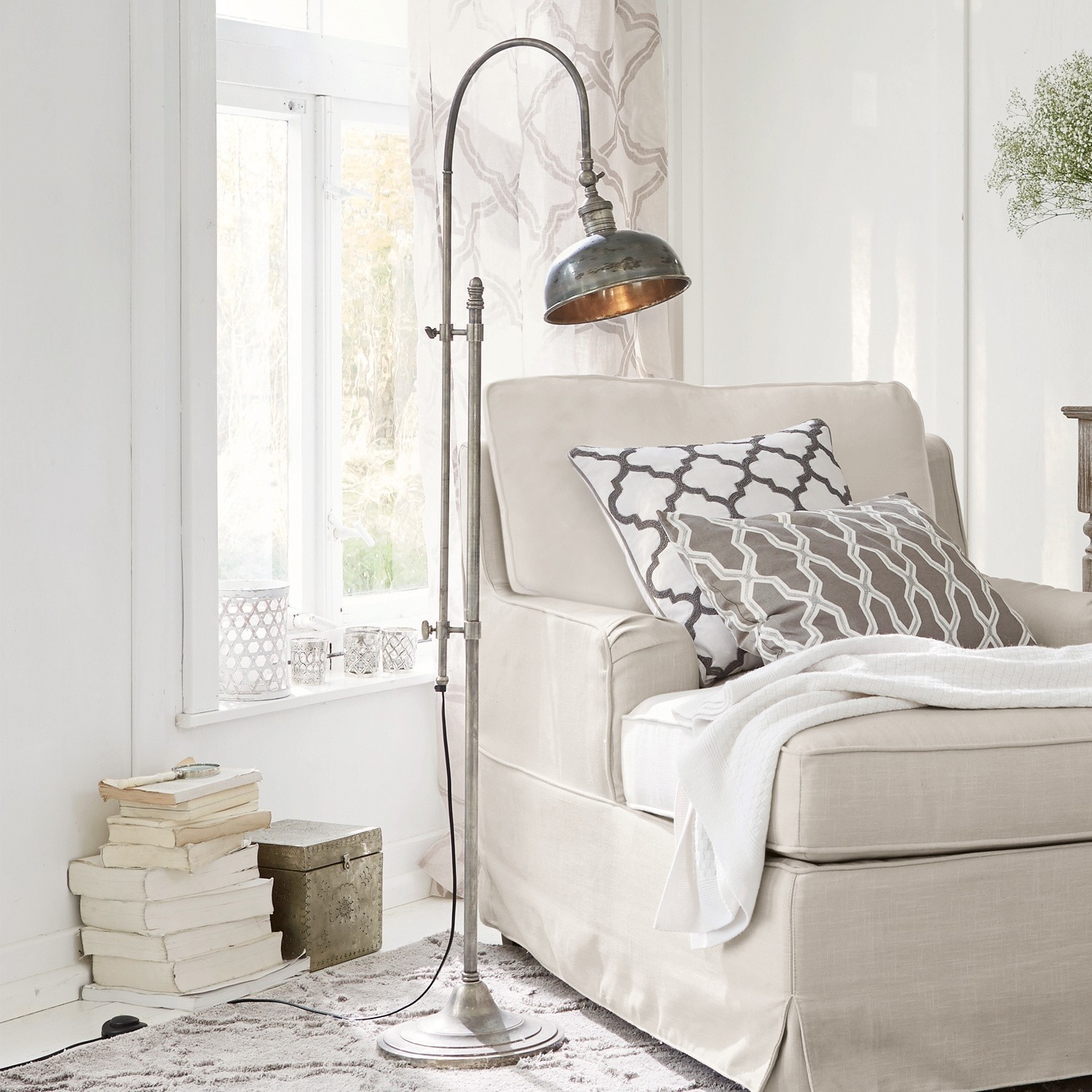 Staande lamp Conway Metalen vintage vloerlamp naast een beige bank met kussens en deken in een lichte woonkamer