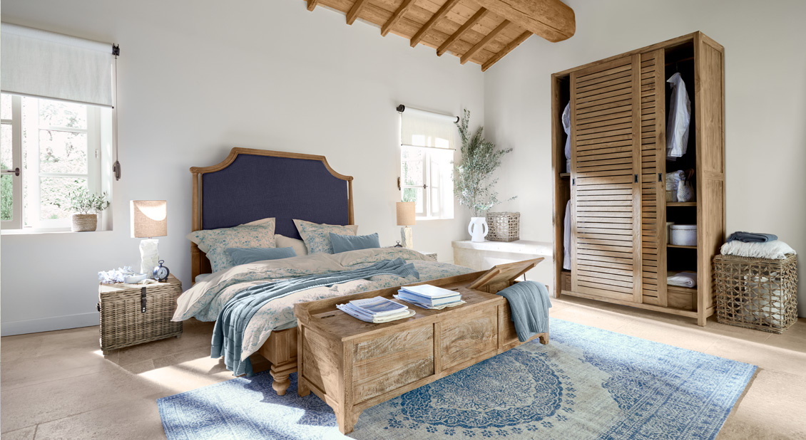 Chambre avec lit en bois et tête de lit bleue, tapis bleu et meubles en bois naturel lumineux