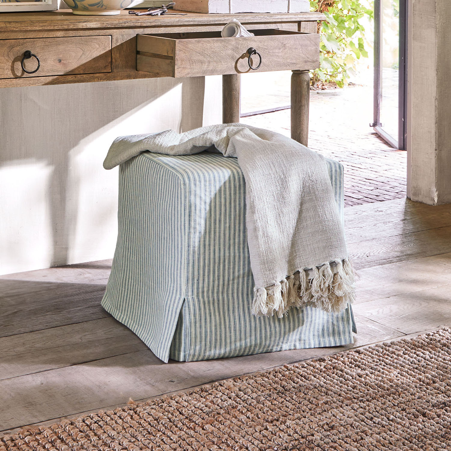 Pouf carré en coton rayé bleu et blanc avec couverture claire à franges sur sol en bois naturel