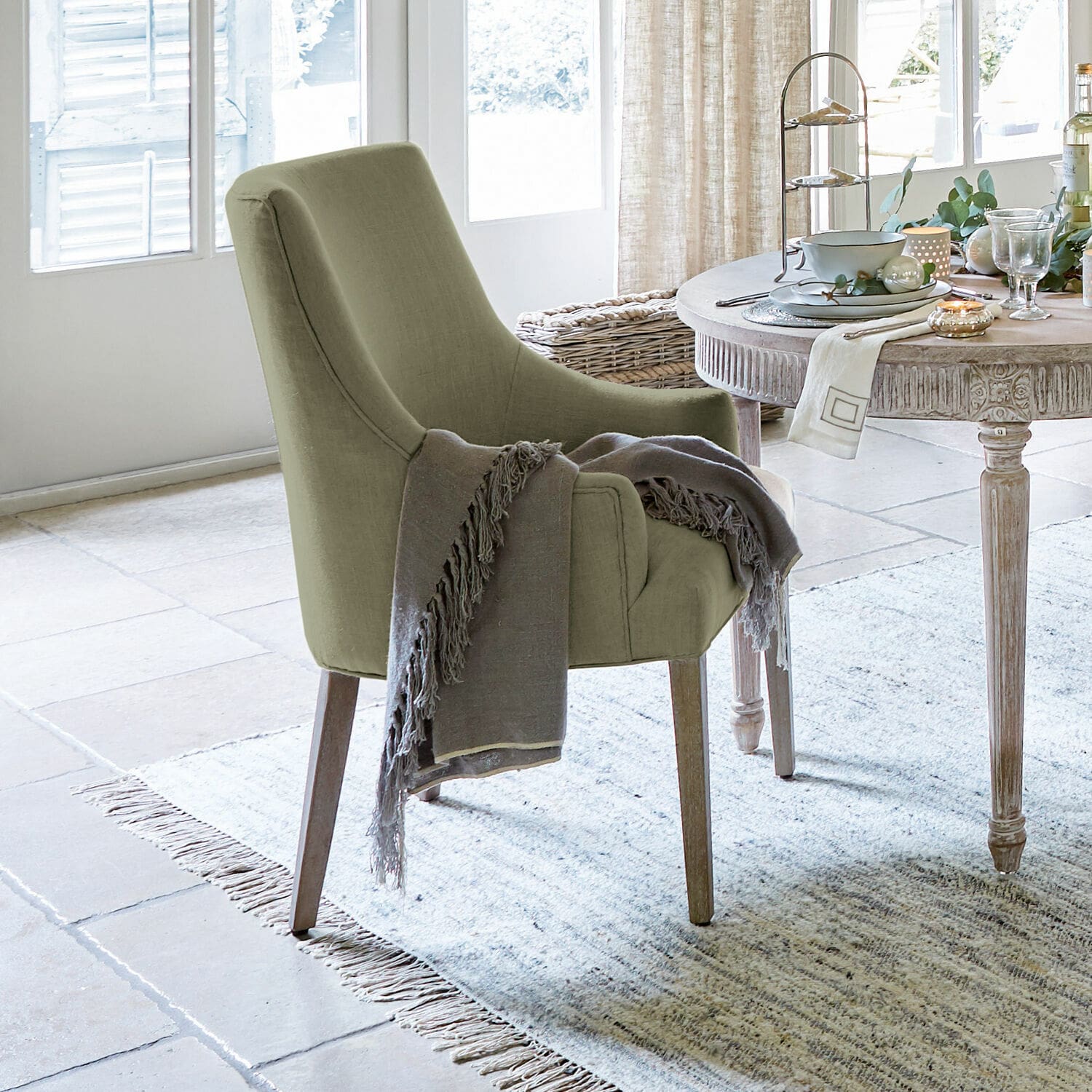 Chaise Hyeres Chaise rembourrée verte avec pieds en bois et plaid gris dans un salon lumineux avec tapis