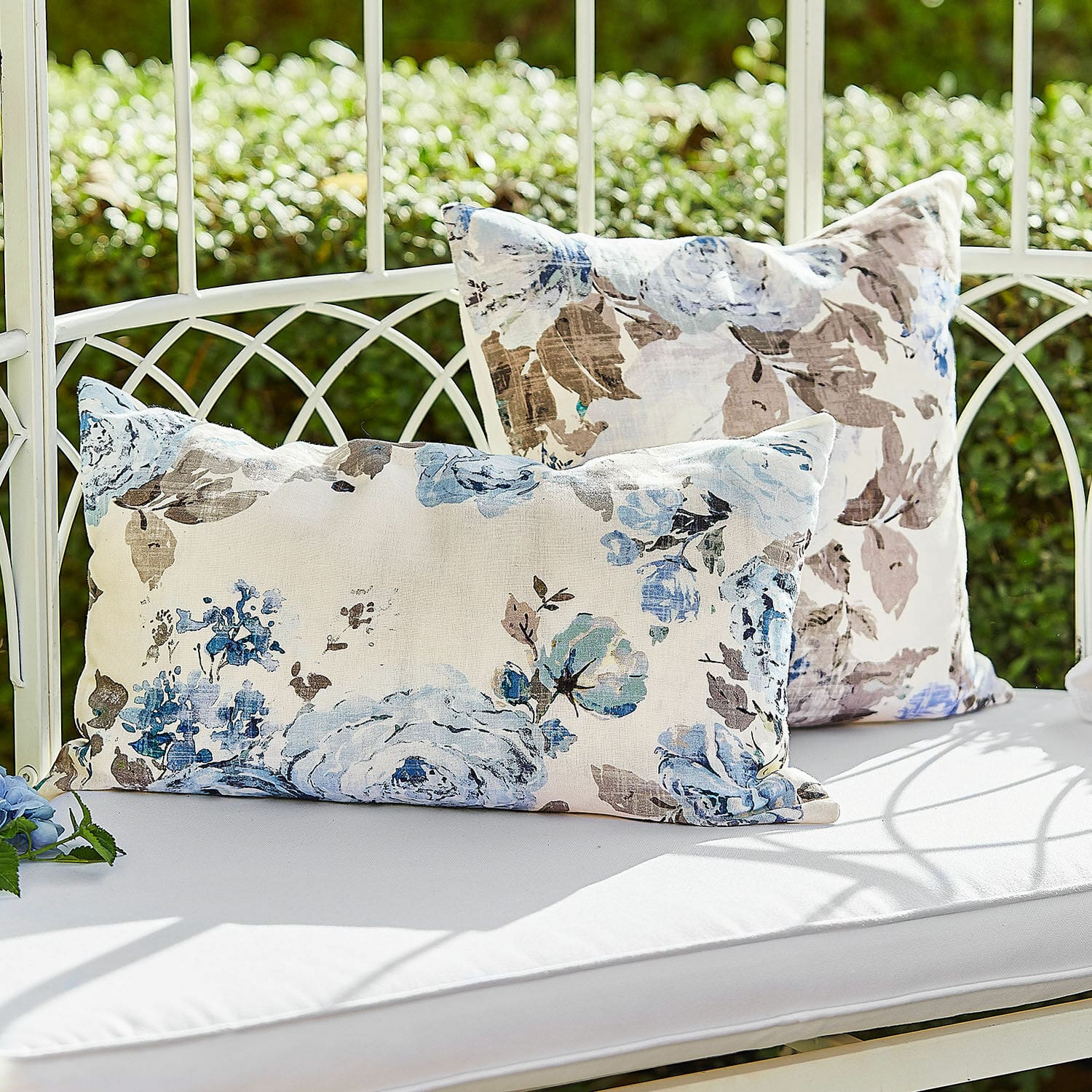 Kussenhoes set van 2 Cloranne Decoratieve katoenen kussens met blauwbruine bloemenprint op een witte tuinbank buiten