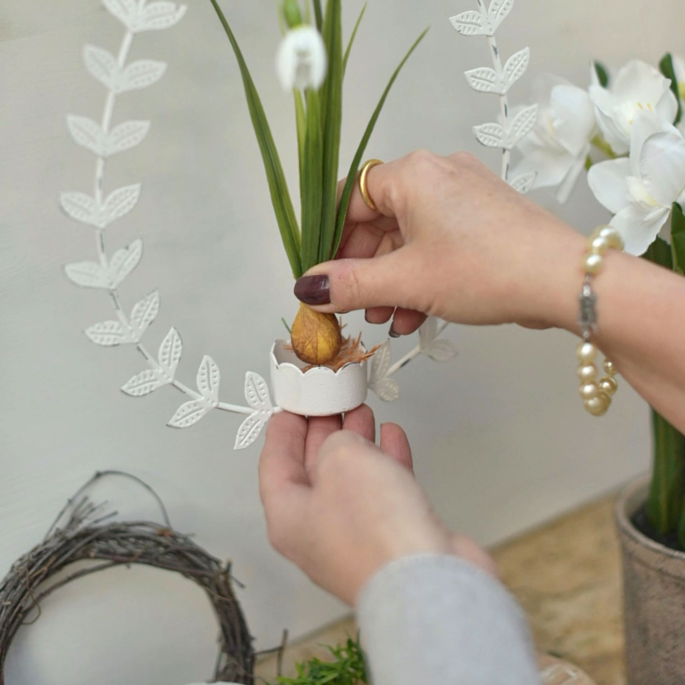 Décoration de Pâques avec couronne métallique blanche et plante verte dans un support en céramique