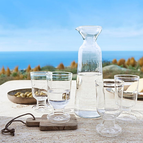 Glazen karaf en vier doorzichtige glazen op tafel met uitzicht op zee, helder glas