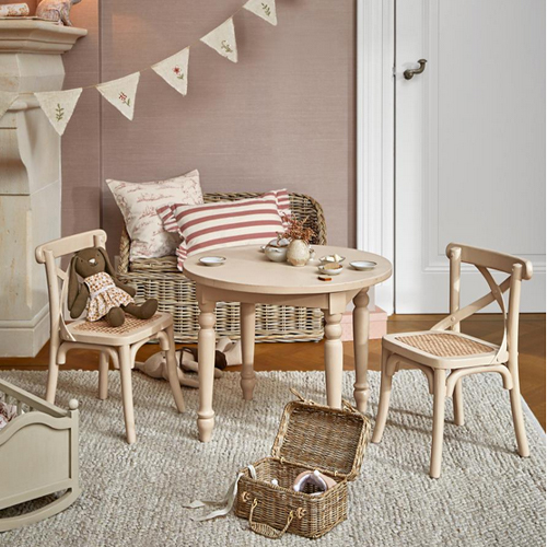 Table ronde en bois clair avec deux chaises et un panier en osier sur un tapis dans une chambre d'enfant lumineuse