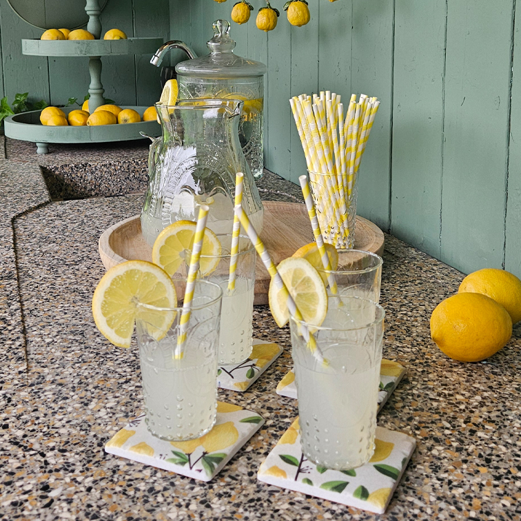 Verres de limonade avec tranches de citron sur un comptoir en pierre avec pailles en papier et plateau de citrons