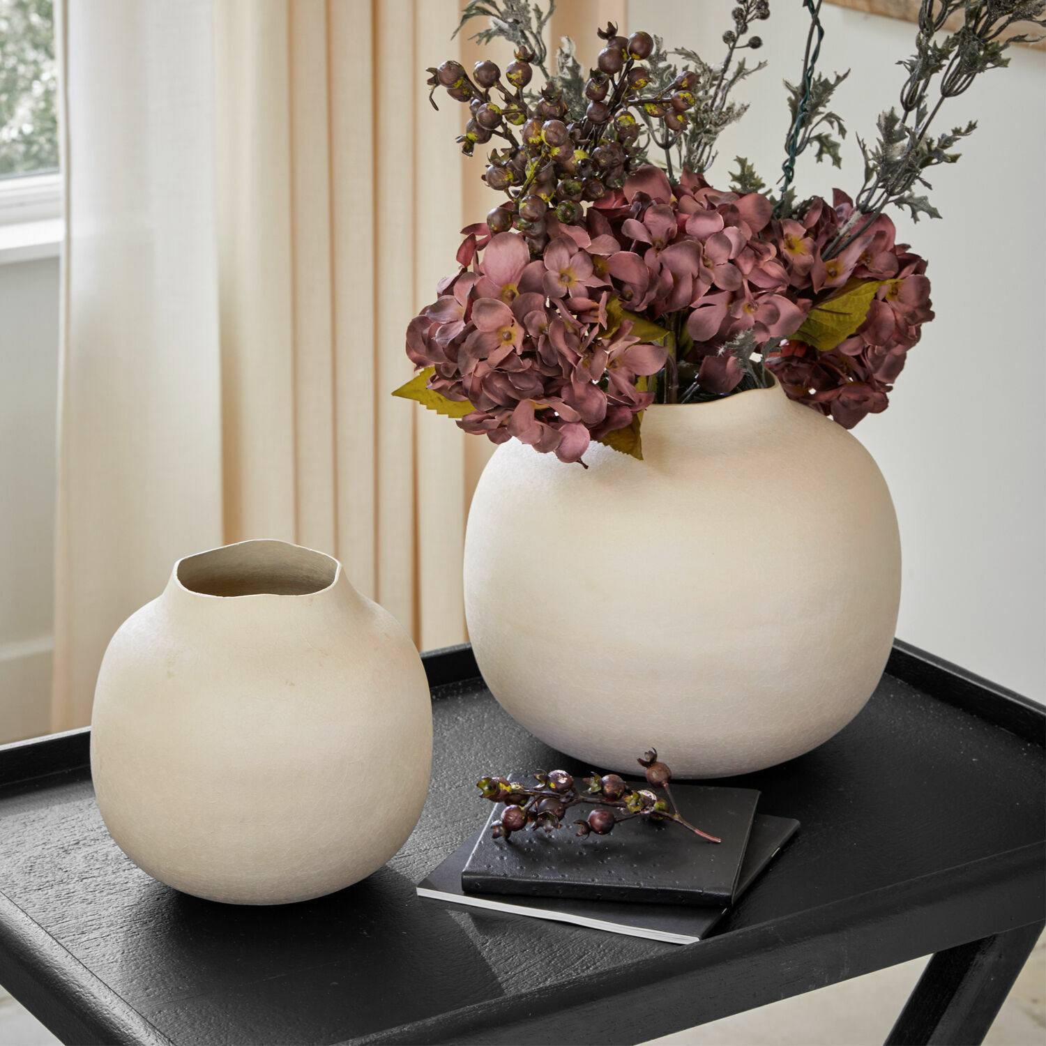 Vaas set van 2 Fleurons Twee crèmekleurige keramische vazen op een zwarte tafel met decoratieve bloemen en boeken op de achtergrond