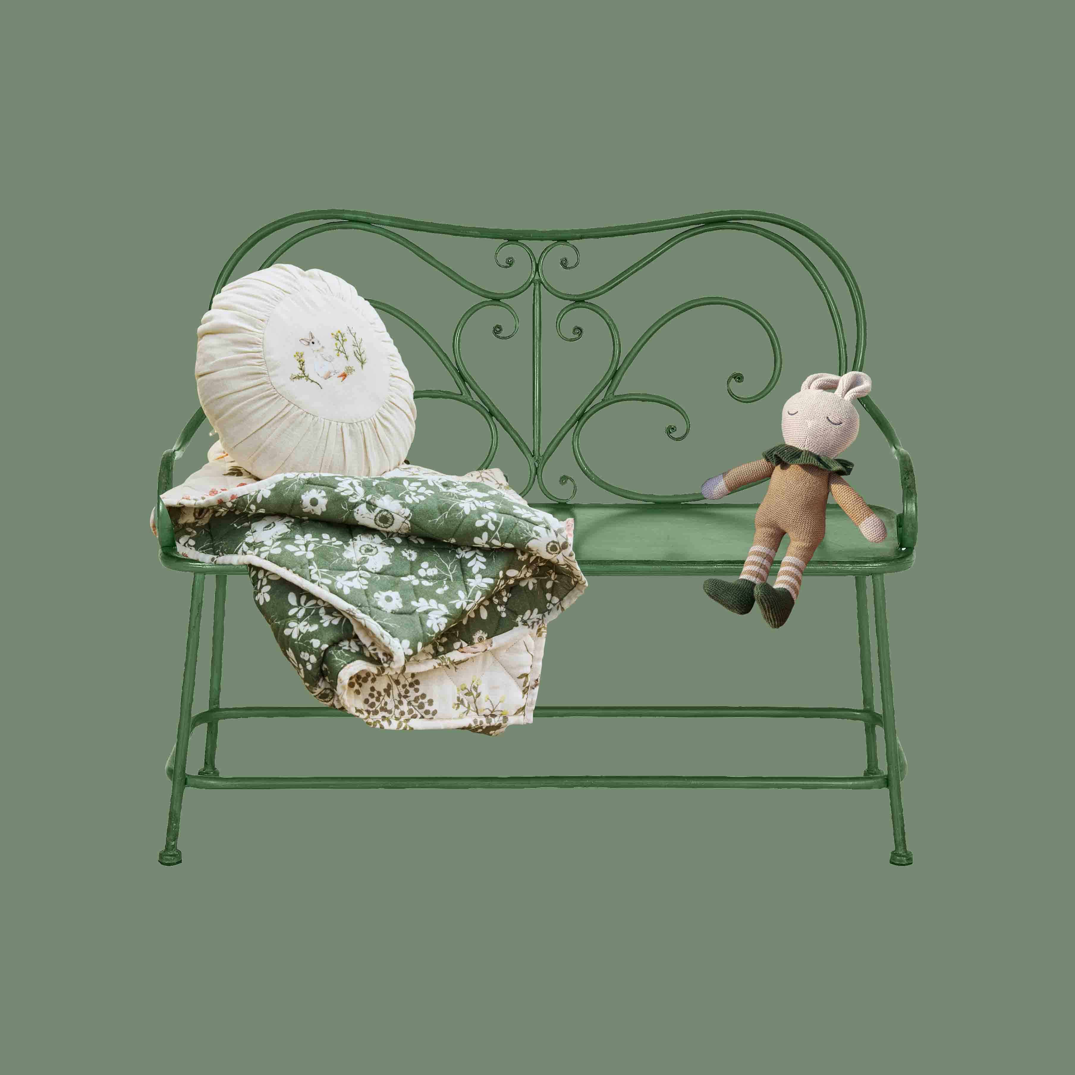 Banc en métal vert avec dossier orné, coussin crème et peluche lapin pour décoration enfant