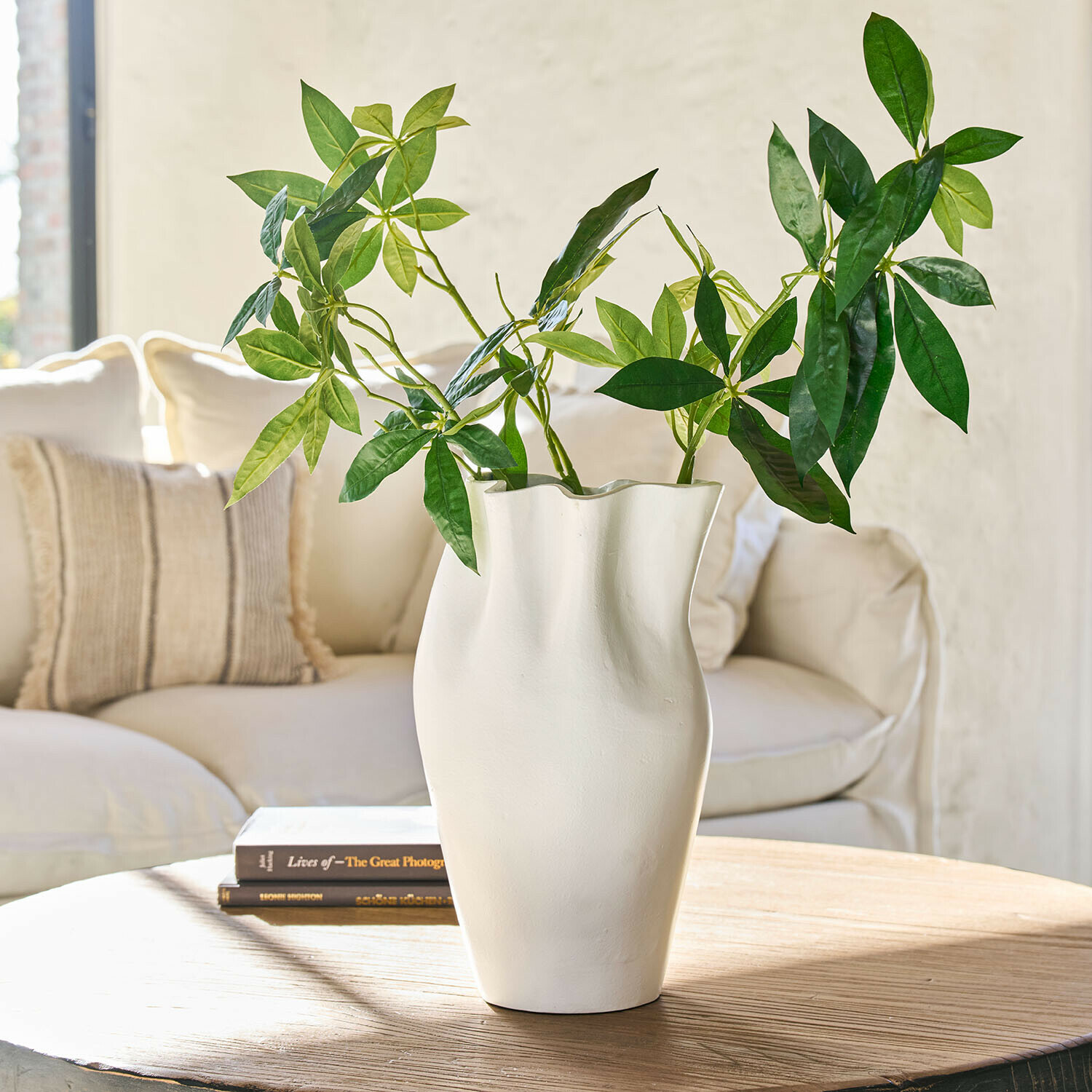 Vase Palomira Vase blanc en céramique à forme ondulée avec feuillage vert sur table en bois dans un salon