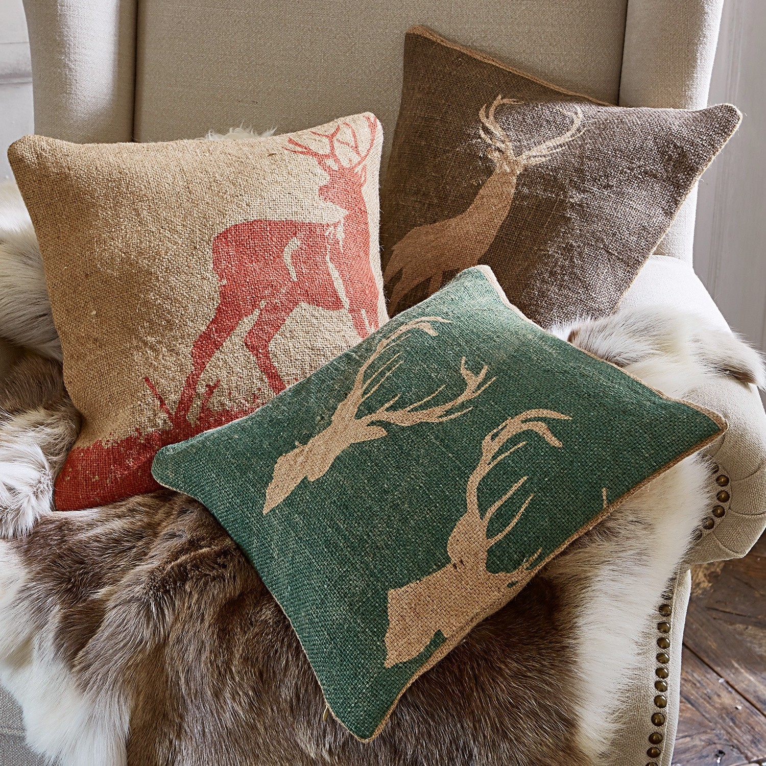 Kussenhoes set van 3 Shrewton Drie decoratieve kussens met hertmotief in natuurlijke kleuren op stoel met bontdeken