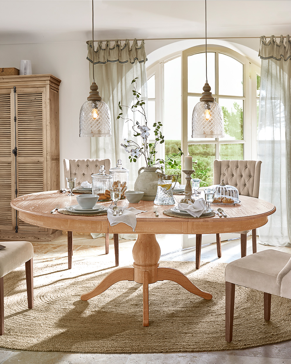 Ovale eettafel van licht hout met beige stoelen en sfeervolle tafeldecoratie in landelijke stijl