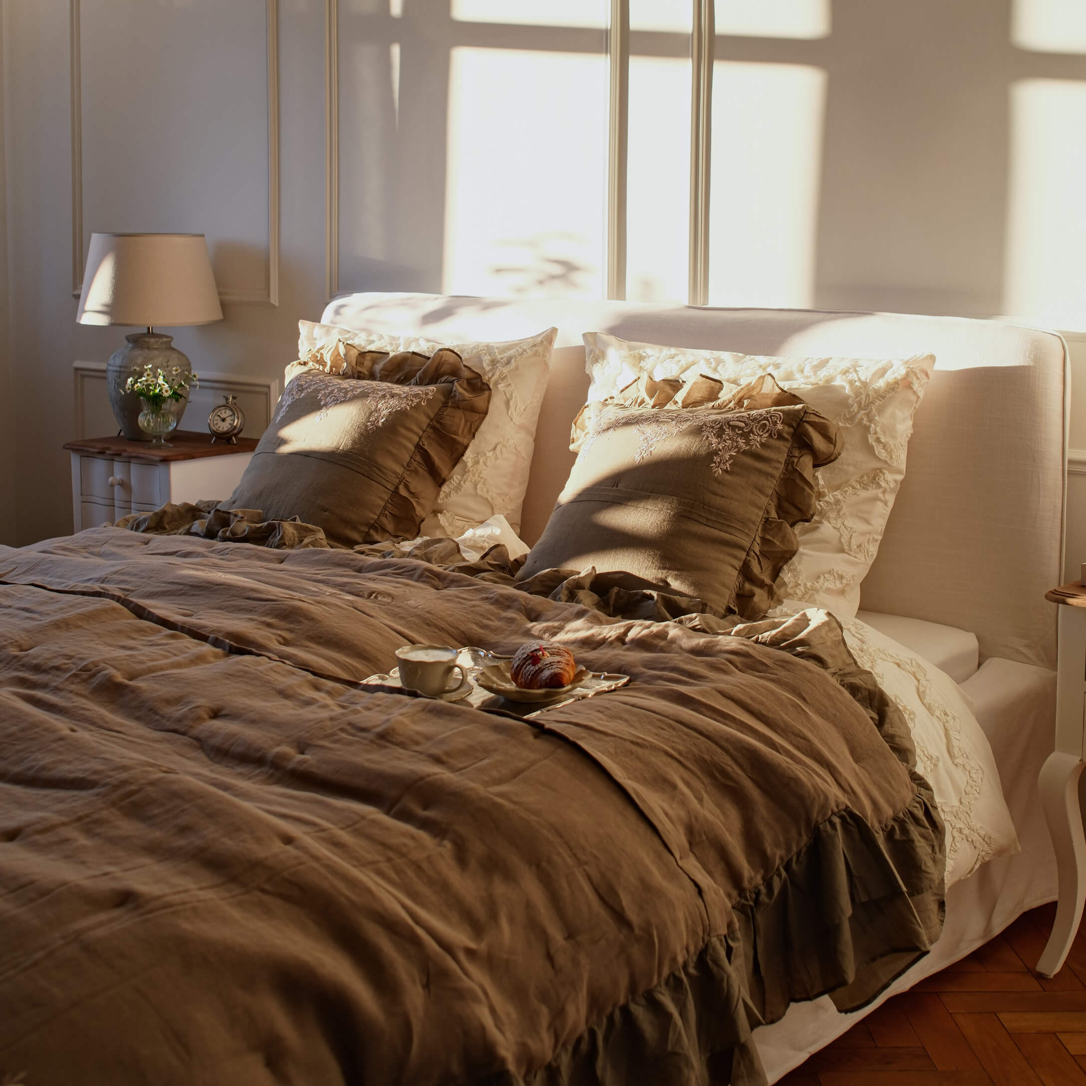 Chambre chaleureuse avec linge de lit en lin beige et coussins à volants marron dans une lumière douce