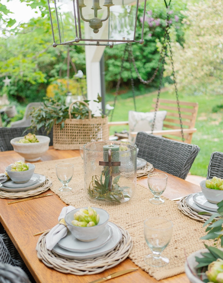 Table de jardin en bois naturel avec sets de table en osier et décoration de bougie dans un vase en verre