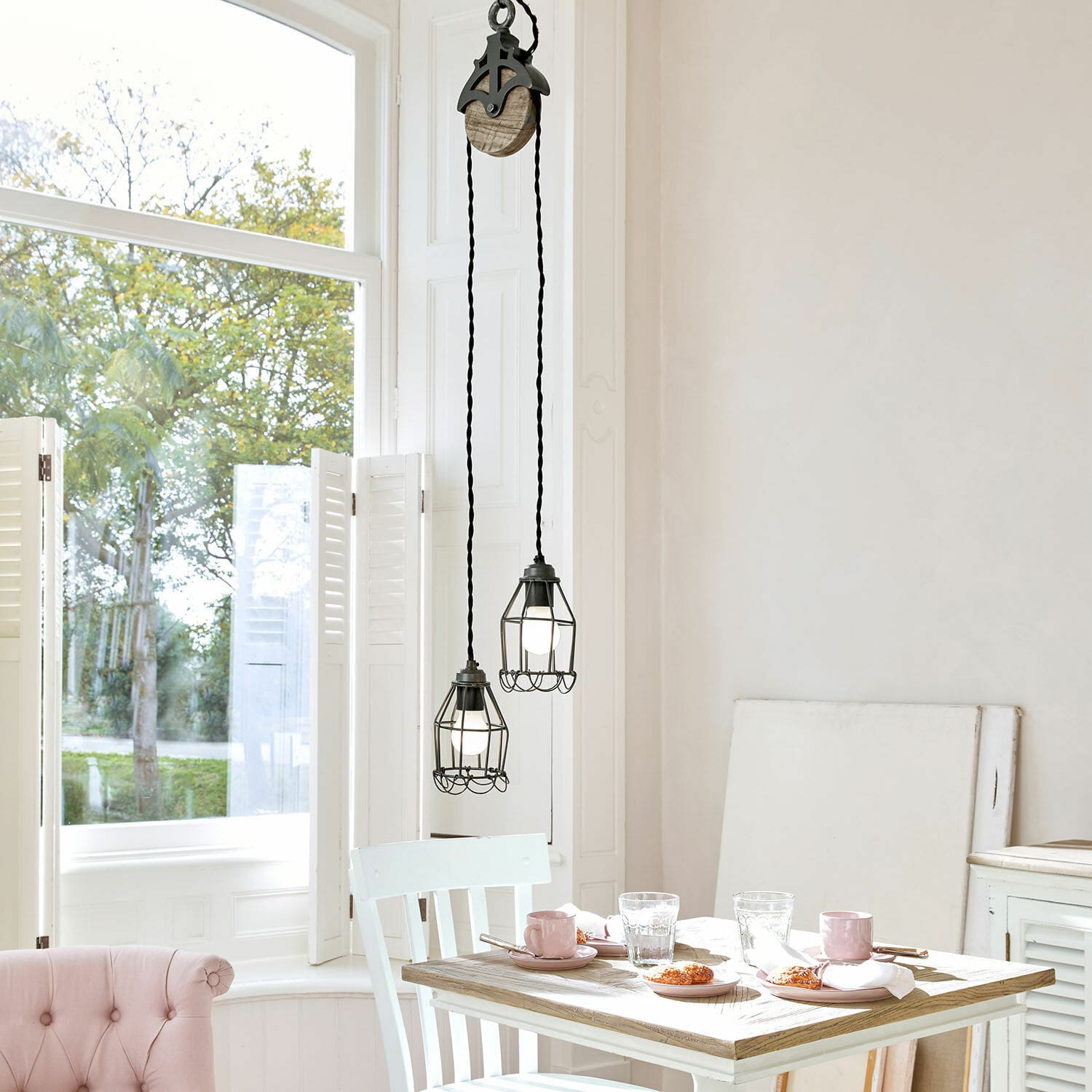 Hanglamp Trevici Twee zwarte metalen hanglampen met beschermkooi boven houten tafel in lichte kamer