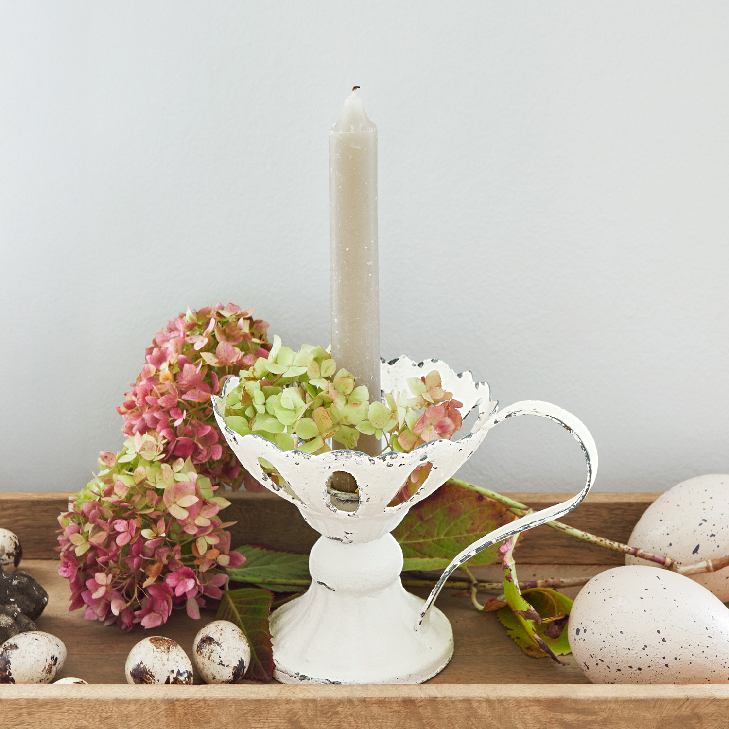 Bougeoir en métal blanc avec anse et bougie grise, décoré de fleurs et d'œufs décoratifs