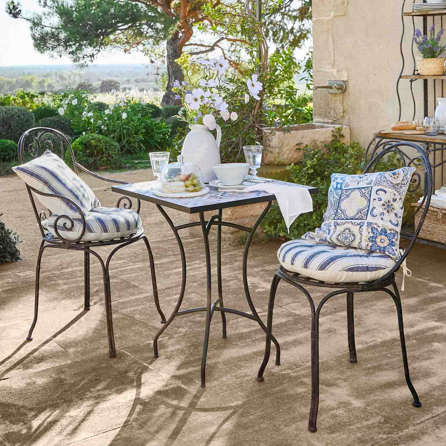 Metalen vierkante tafel met twee stoelen met blauwe kussens op zonnig tuinterras