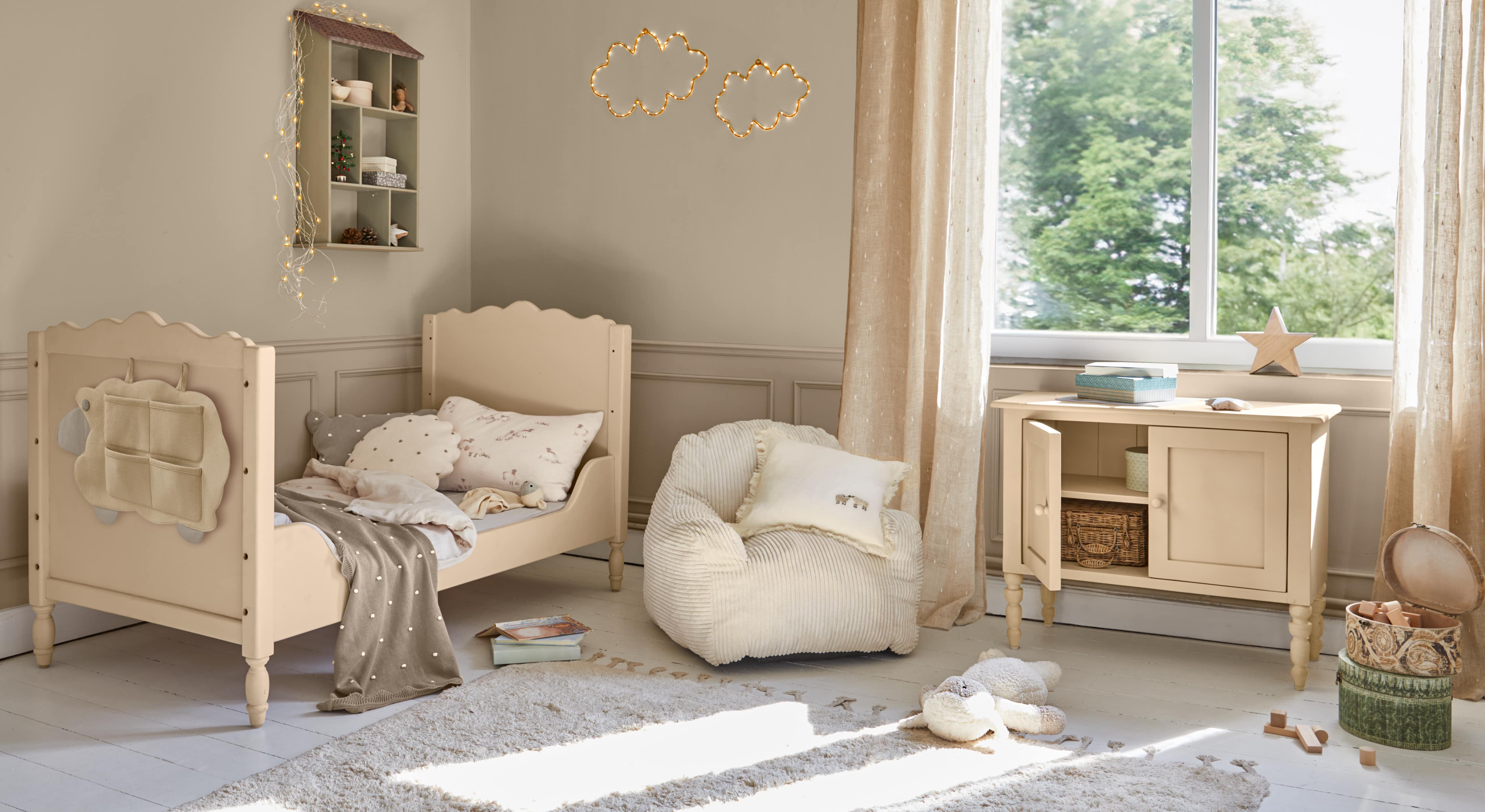 Lit enfant en bois beige avec coussins doux et commode assortie dans une chambre lumineuse