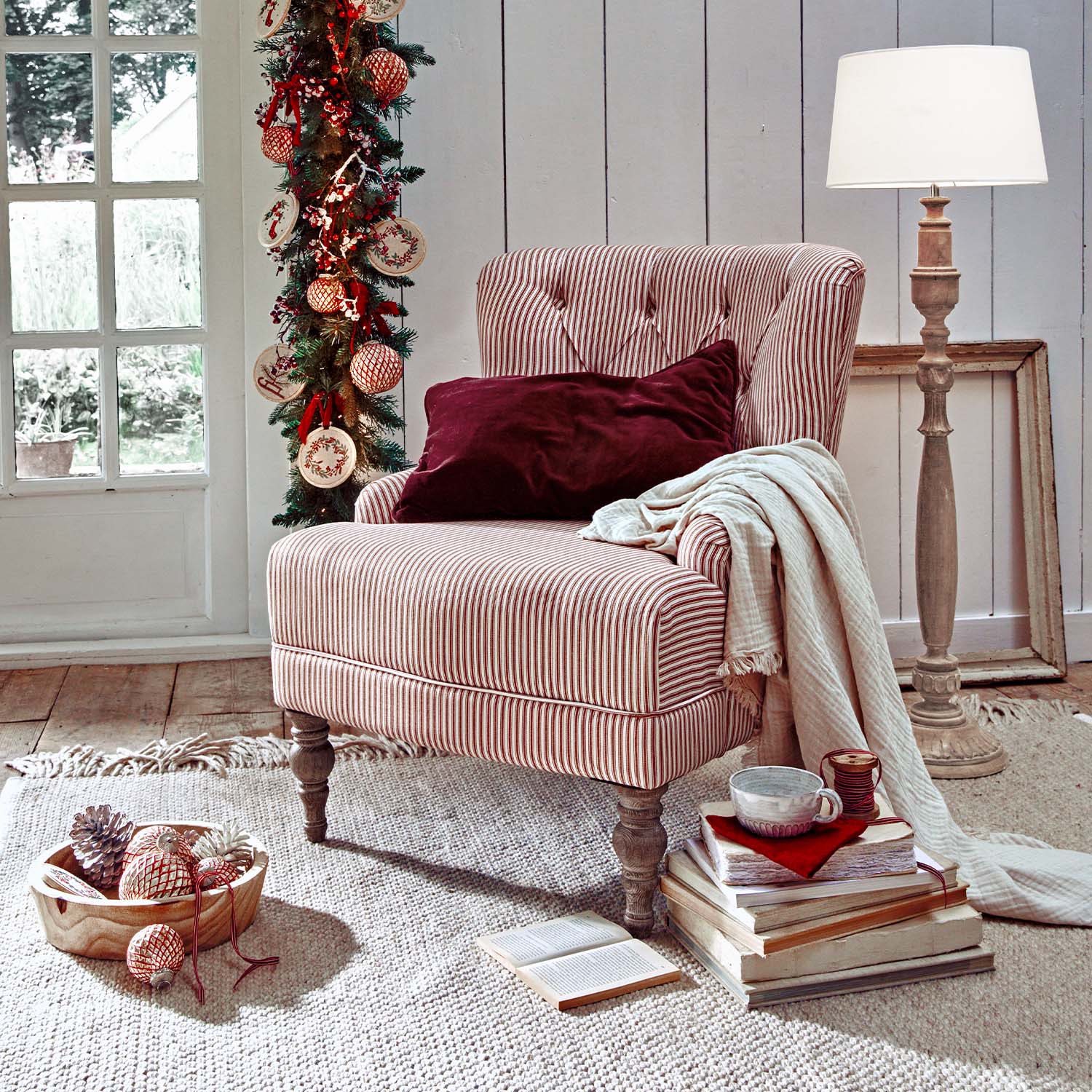 Fauteuil capitonné rayé rouge et blanc avec coussin bordeaux et plaid crème dans un intérieur cosy