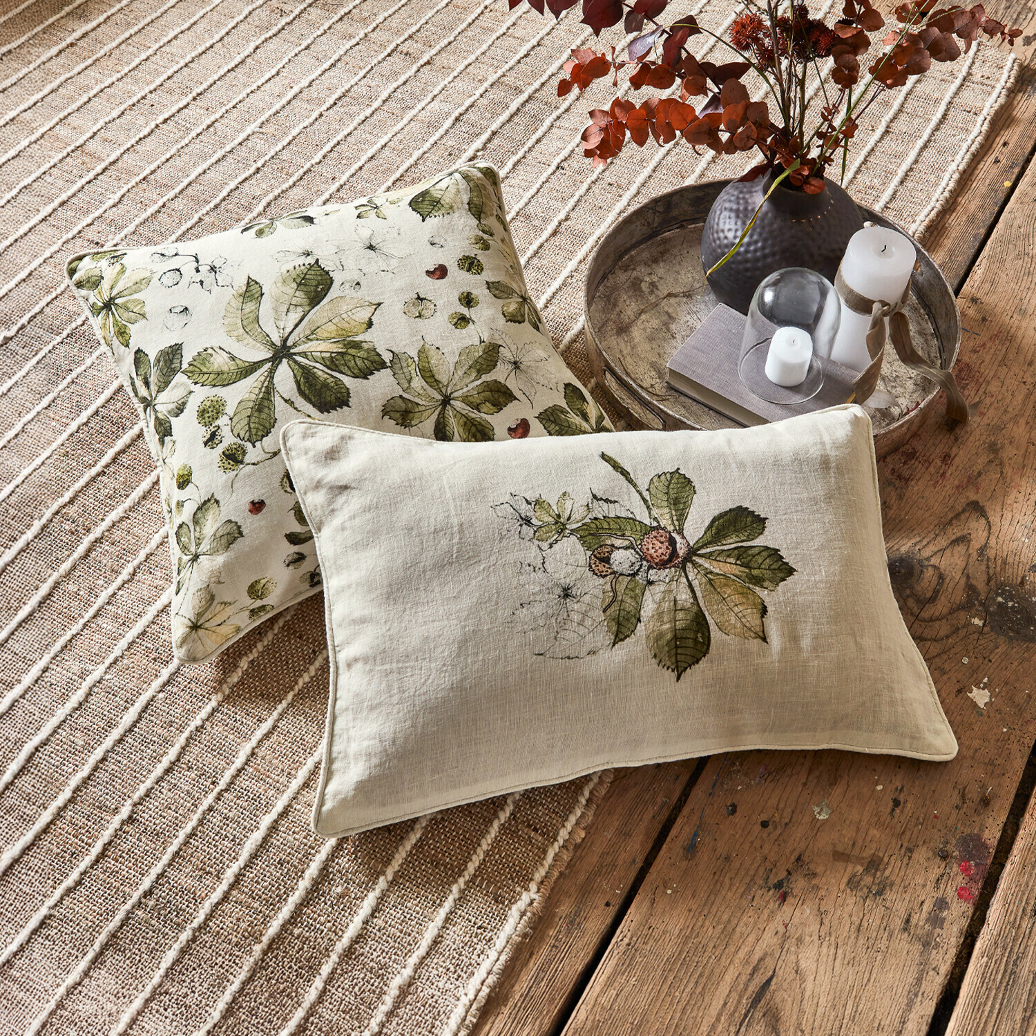 Lot de 2 housses de coussins Elsie Coussins décoratifs en lin avec motifs de feuilles vertes sur fond beige posés sur tapis et plancher en bois
