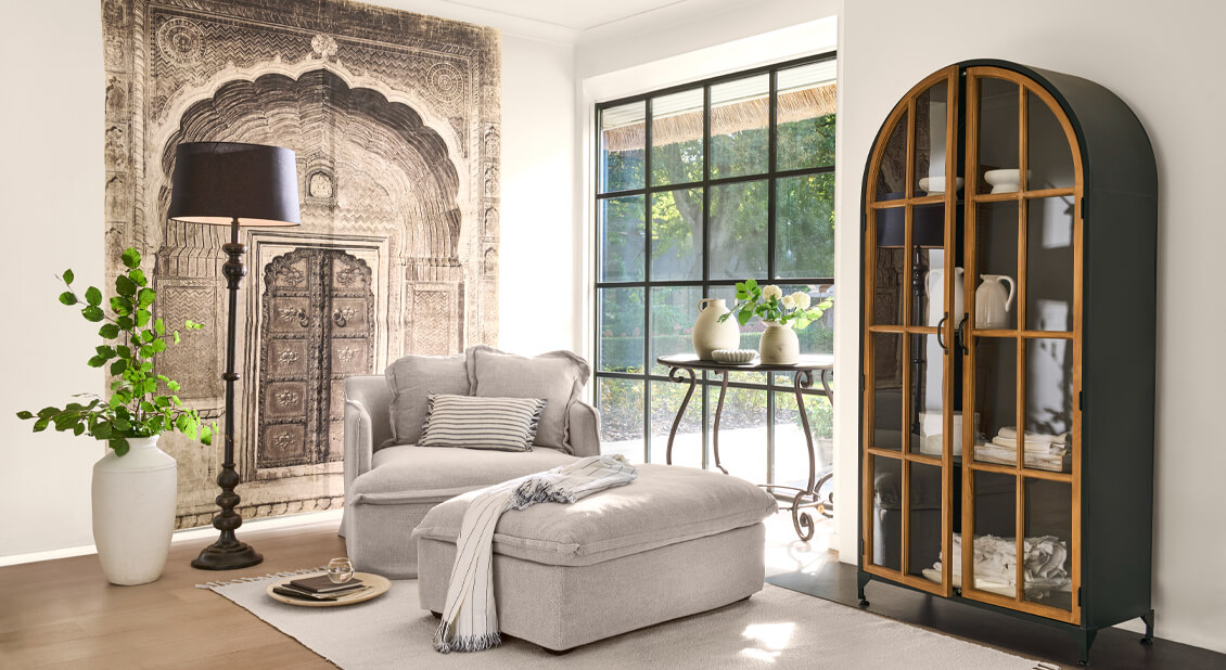 Gezellige woonkamer met beige fauteuil en poef, metalen kast met houten deuren en decoratief wandkleed