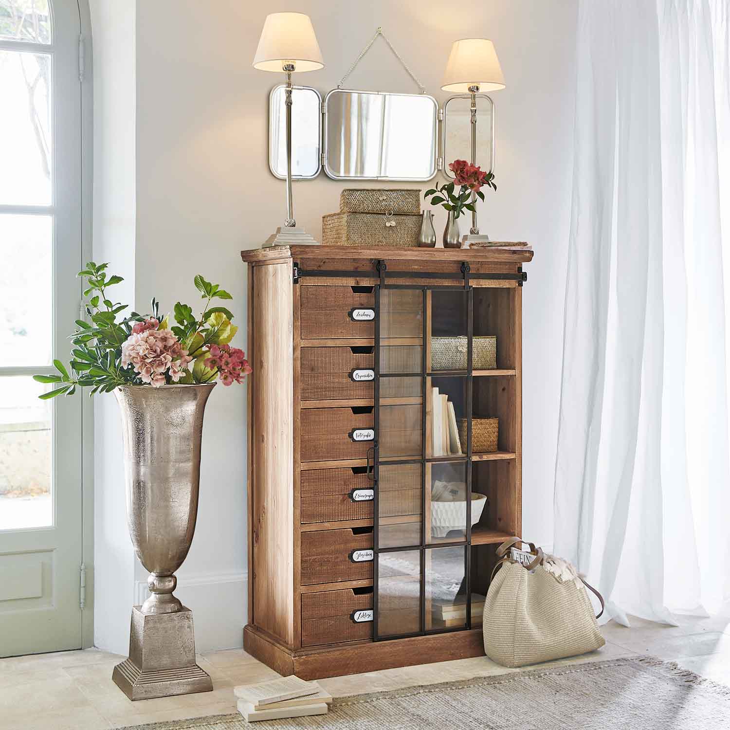 Houten ladekast met glazen deur in lichte kamer met decoraties en lampen